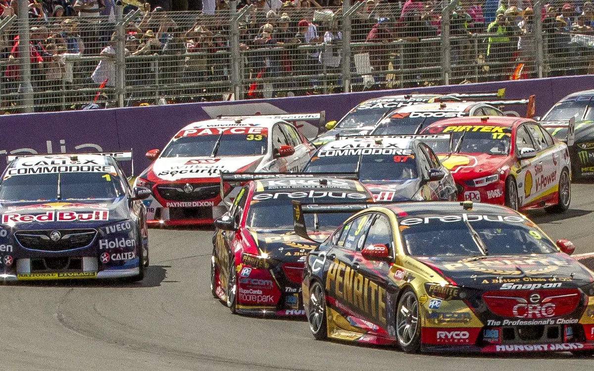 A pack of Supercars racing wheel to wheel at Bathurst in front of a packed crowd